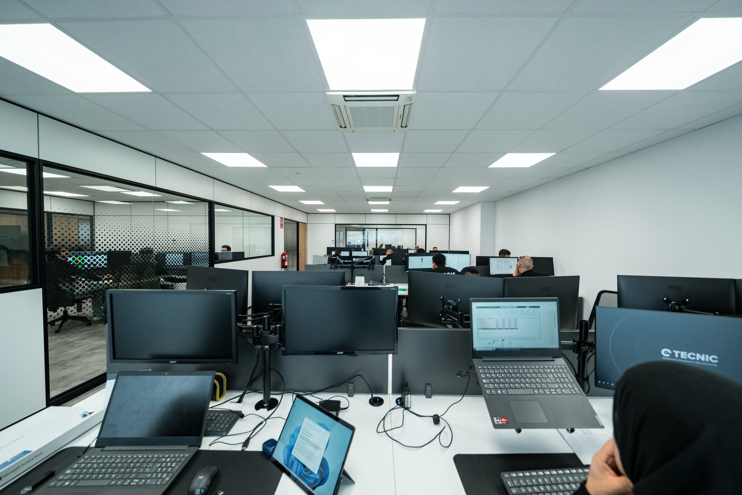 Photo d'un open space avec des postes de travail et des personnes travaillant sur des ordinateurs
